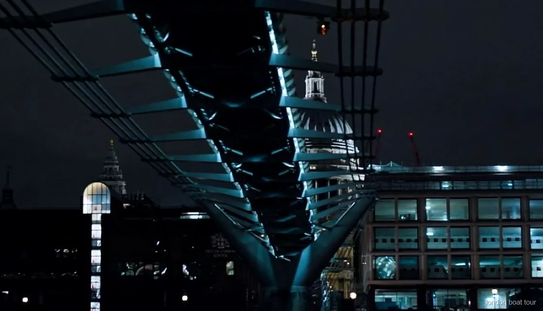 Passagers sur un bateau de croisière de nuit passant devant un pont illuminé de la Tamise