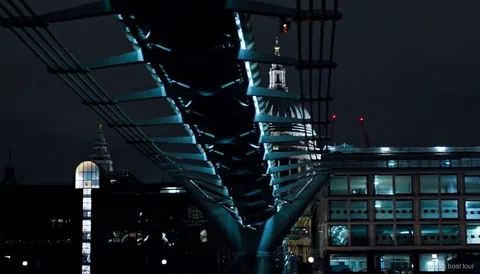 Pasajeros en un crucero nocturno pasando junto a un puente iluminado del Támesis