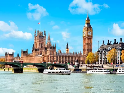 Passageiros no deque aberto de um barco de cruzeiro no Tâmisa com o horizonte de Londres ao fundo