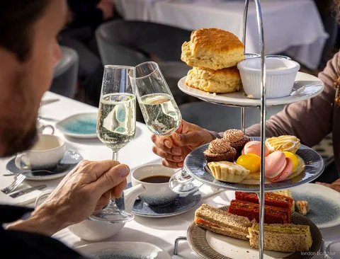 Goście przy stoliku na łodzi podczas rejsu po Tamizie z afternoon tea i widokiem na rzekę