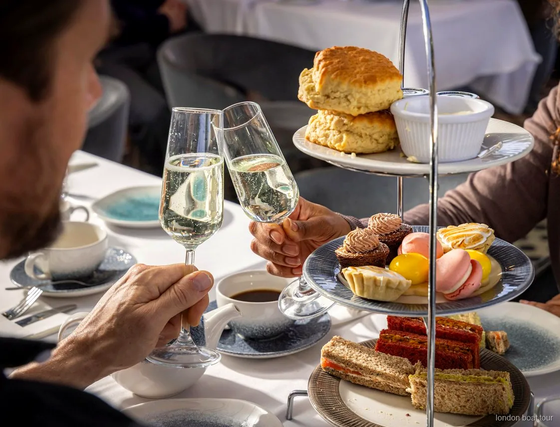 Goście przy stoliku na łodzi podczas rejsu po Tamizie z afternoon tea i widokiem na rzekę