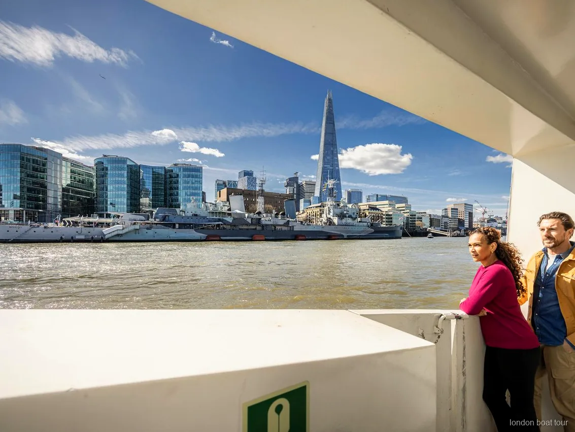 Arkasında Londra yapıları olan Thames hop-on hop-off gezinti turunda açık güverte oturma alanı