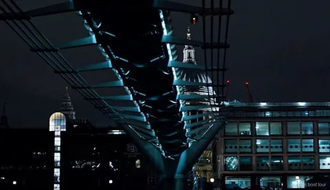 Passengers on an illuminated night cruise boat passing a lit-up Thames bridge