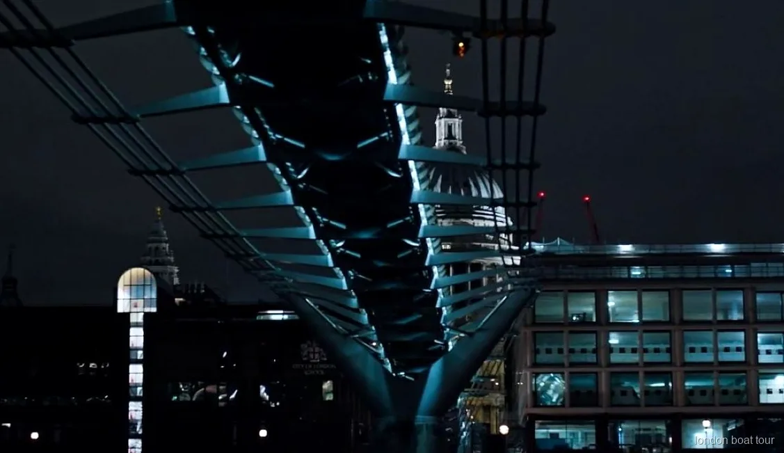 Passengers on an illuminated night cruise boat passing a lit-up Thames bridge