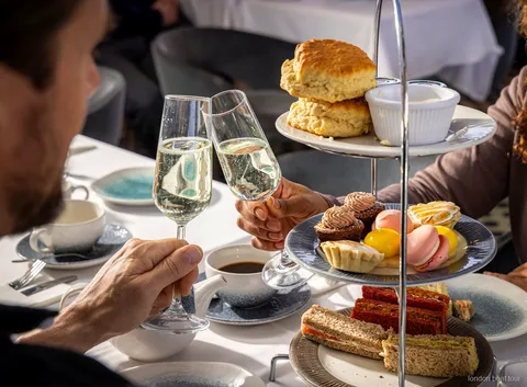 Gæster sidder ved et bord på en afternoon tea sejltur på Themsen med udsigt over floden